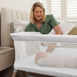 Mum attending to her baby, from her bed while baby is safe in bedside crib, with zipped window down.