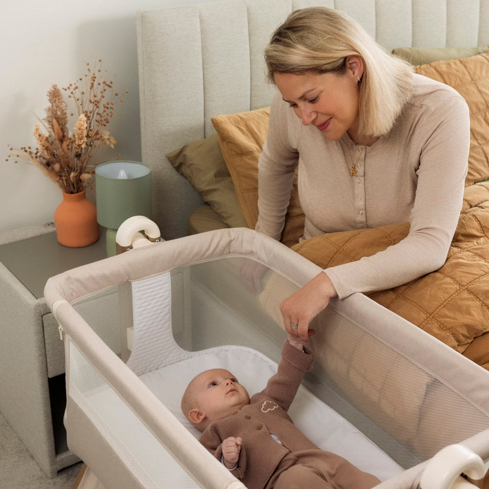 Baby in bedside crib holding on to mum's hand while shes in her own bed