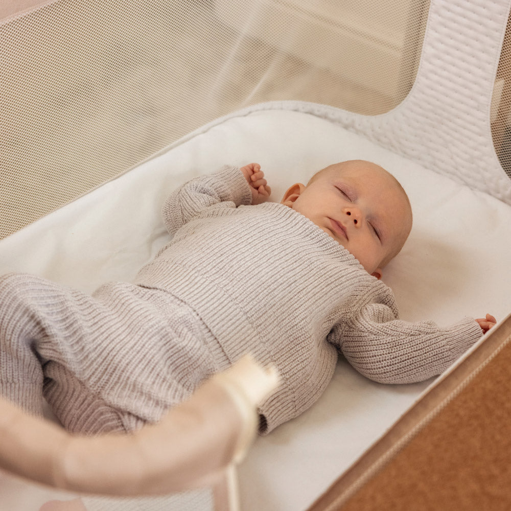 Baby sleeping in bedside crib with side panel lowered.