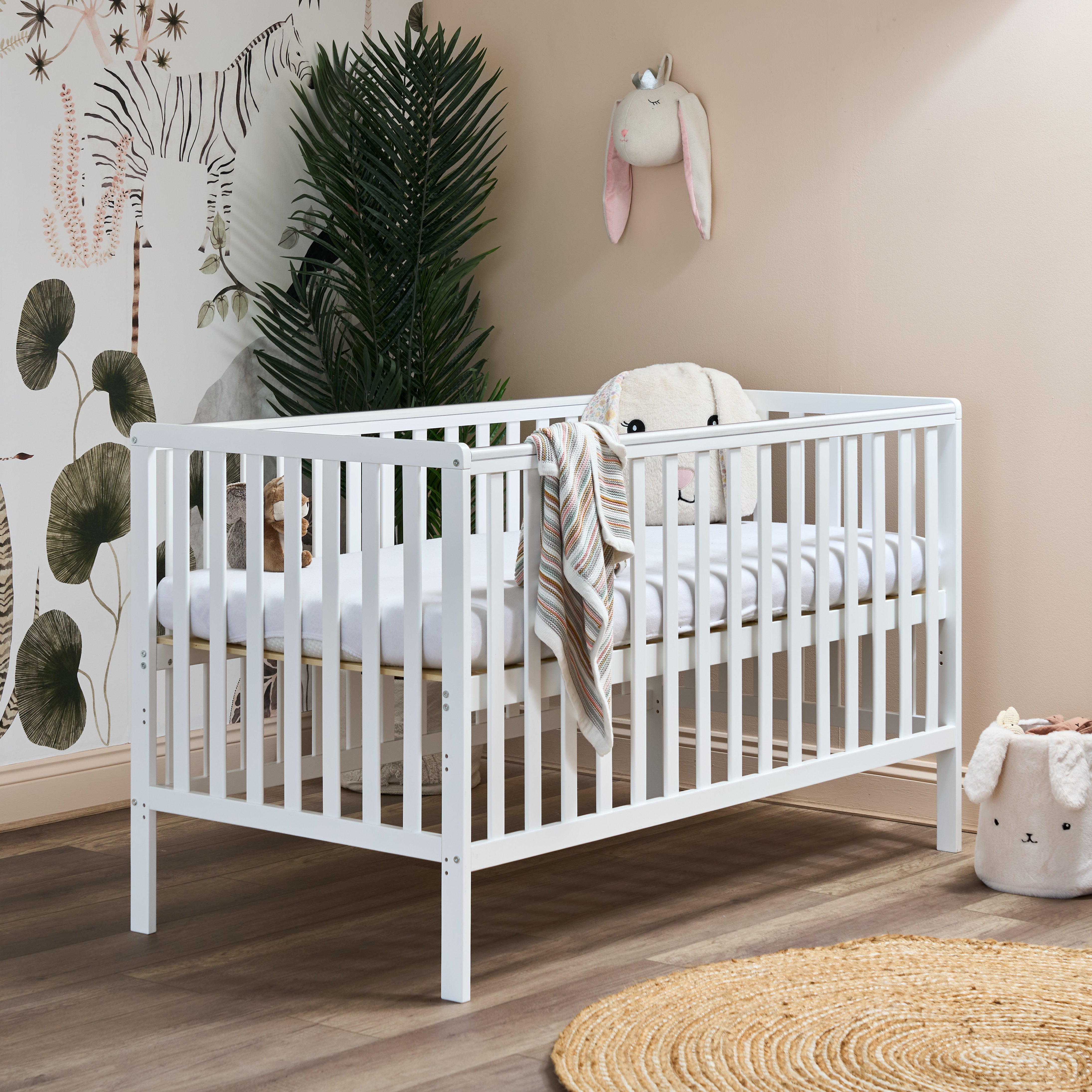white cot bed, with rails on all 4 sides, teething rails on the longest sides, base on the new born setting for easy access for parents to lean in.