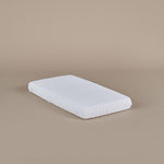 White baby cot mattress on a beige background, showing fitted sheet 