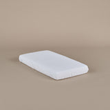 White baby cot mattress on a beige background, showing fitted sheet 