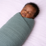 Newborn baby swaddled in a muslin green/turquoise blanket on a white background