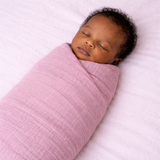 Newborn baby swaddled in a pink/berry muslin blanket on a white background