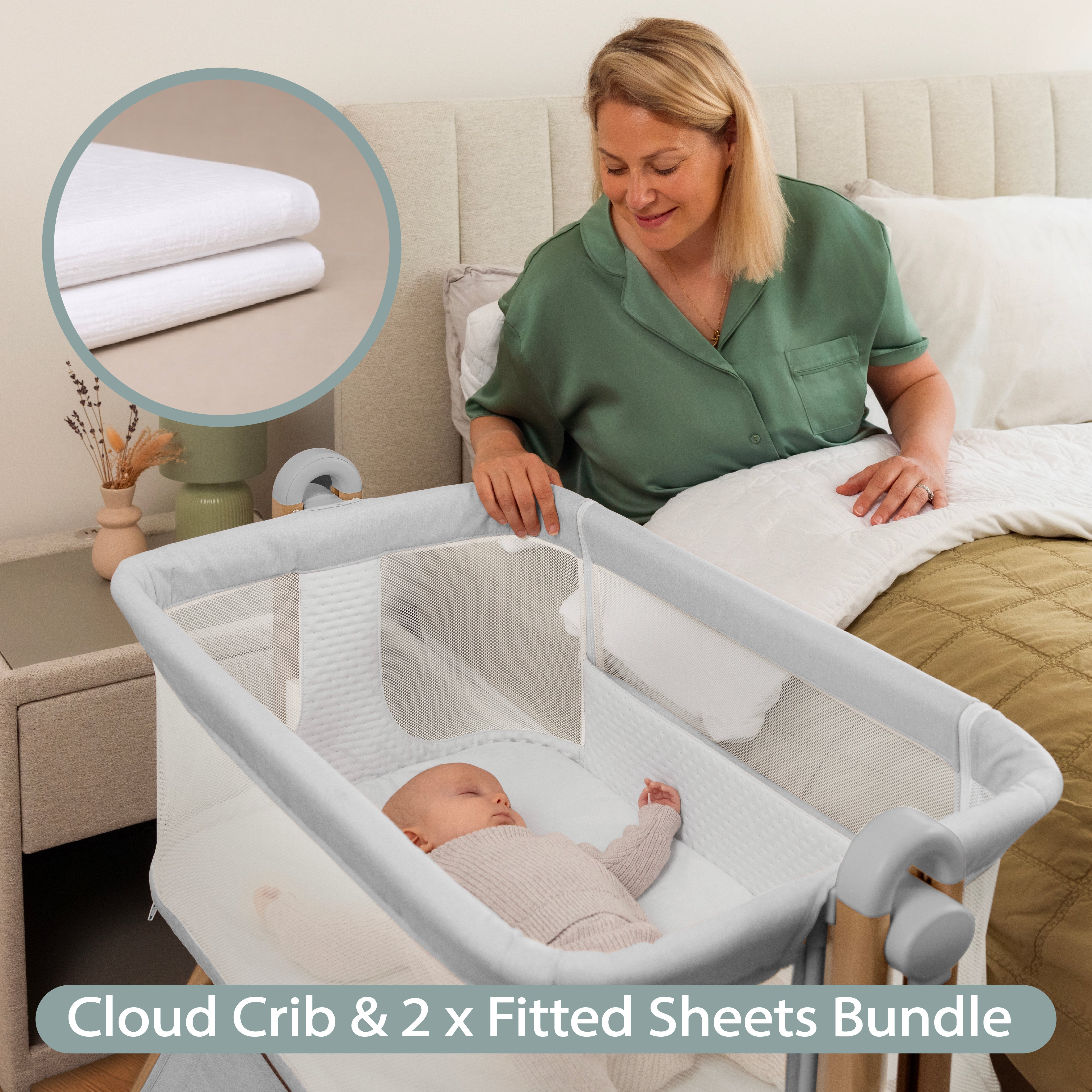 Grey Bedside crib with wood effect frame. mesh sides, with sleeping baby in crib & mum looking on from her own bed & mini shot of muslin fitted sheet.