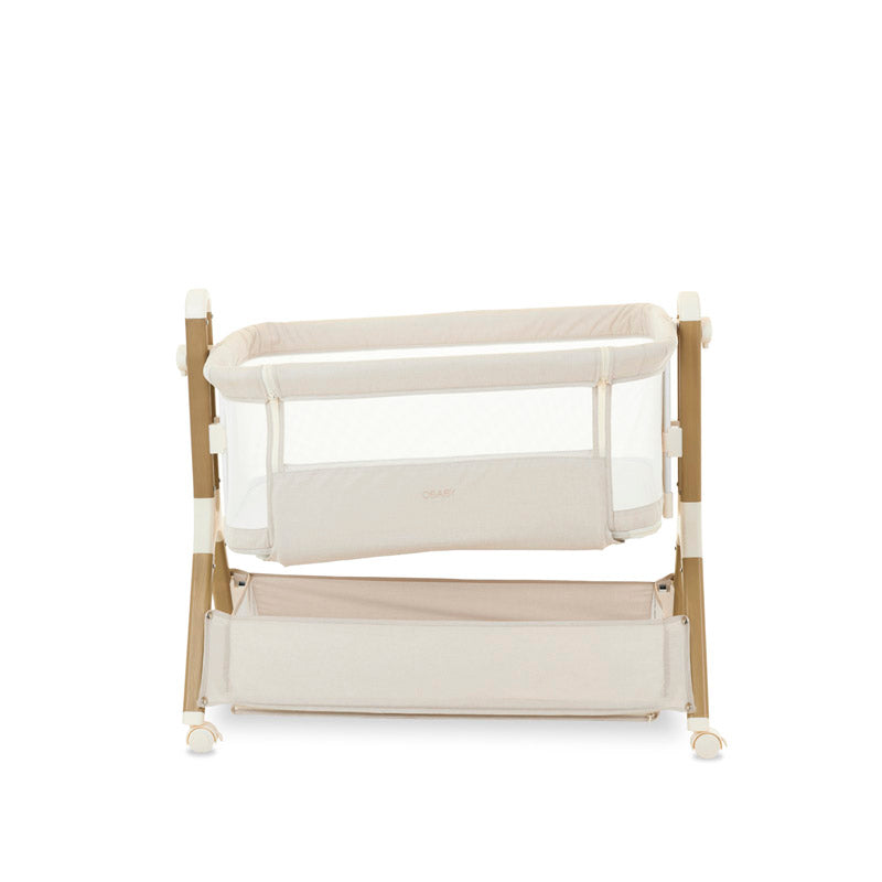 Bedside crib, in oatmeal with wood effect frame, crib positioned on a tilt to help with colic, storage basket underneath the crib.
