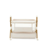 bedside crib, with fabric oatmeal, mesh sides, wood effect frame, crib on lowest setting, storage basket underneath crib for parent easy access. 