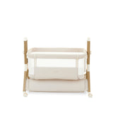 Bedside crib on its lowest setting, with oatmeal fabric, wood effect frame, storage basket underneath crib. Caster wheels to help move the crib into position 