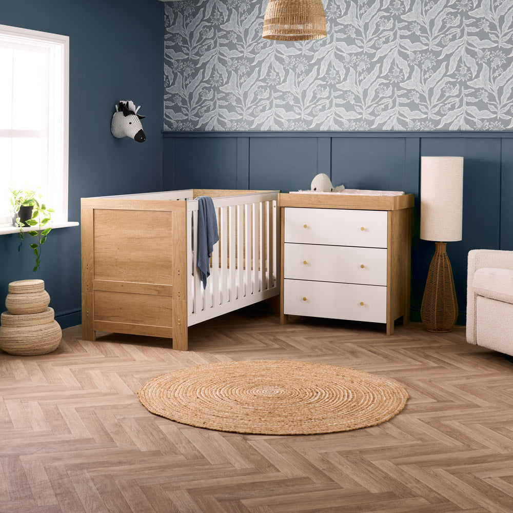 2 Piece nursery set in oak & white includes a cot bed with oak effect & white rails and white dresser with 3 drawers front with gold round handles. 