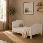 cot bed in toddler bed mode. slatted ends finished with curve tops in nursery setting, 