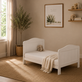 cot bed in toddler bed mode. slatted ends finished with curve tops in nursery setting, 